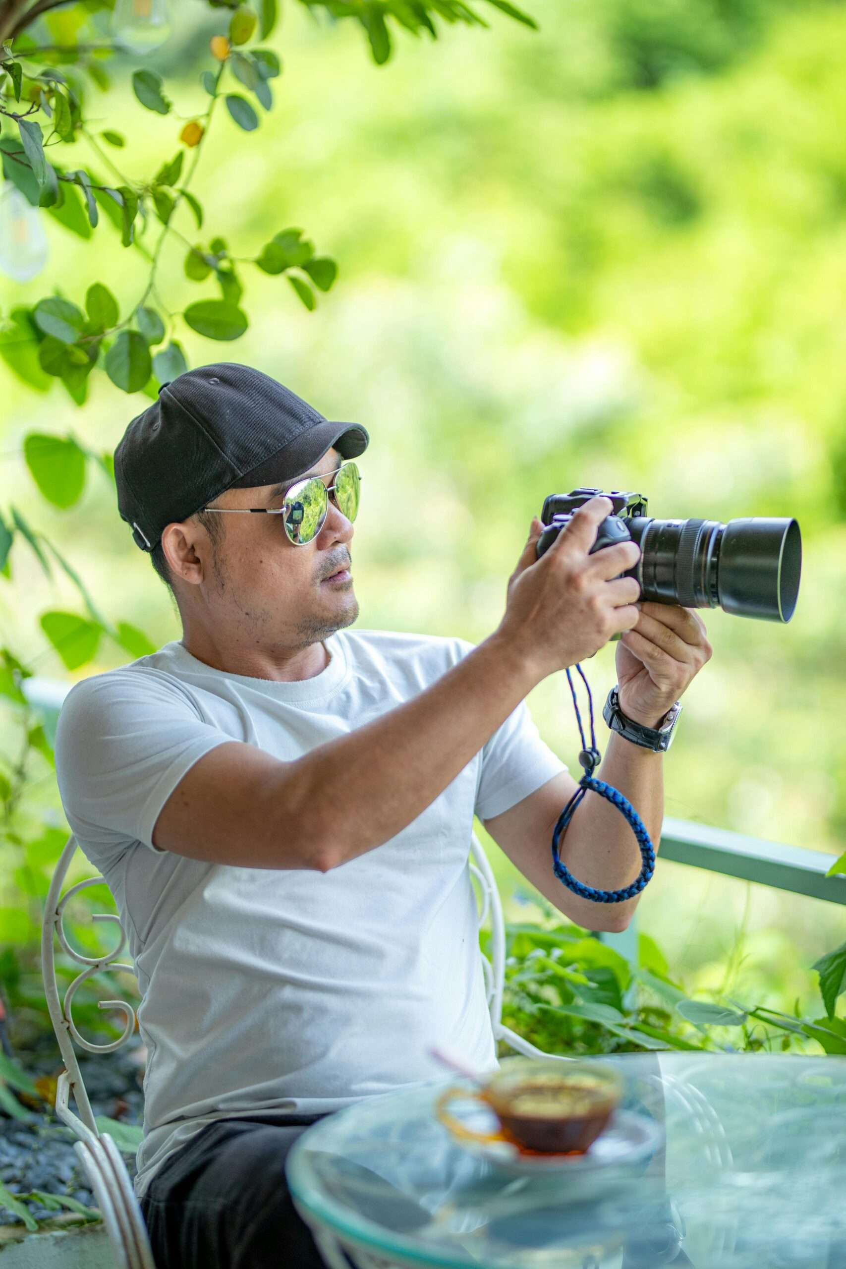 Man in white shirt using a camera outdoors, surrounded by greenery.